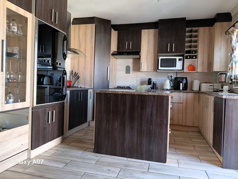 A modern kitchen featuring two-tone cabinetry, granite countertops, a central island, built-in oven, and extractor fan with tiled flooring throughout.