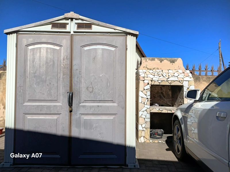 Outdoor area featuring a built-in braai with mosaic tile detailing and a standalone storage shed on a paved surface.