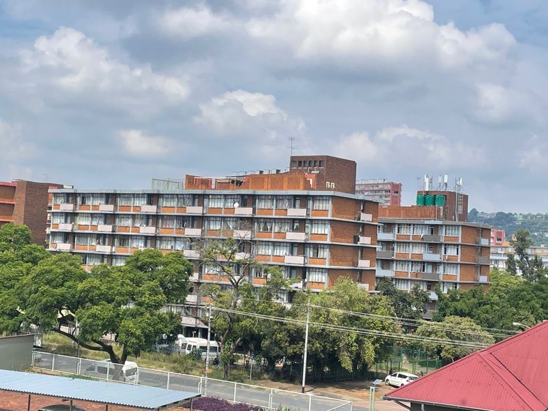 An elevated exterior view of a multi-story brick apartment complex featuring rows of balconies and large windows.