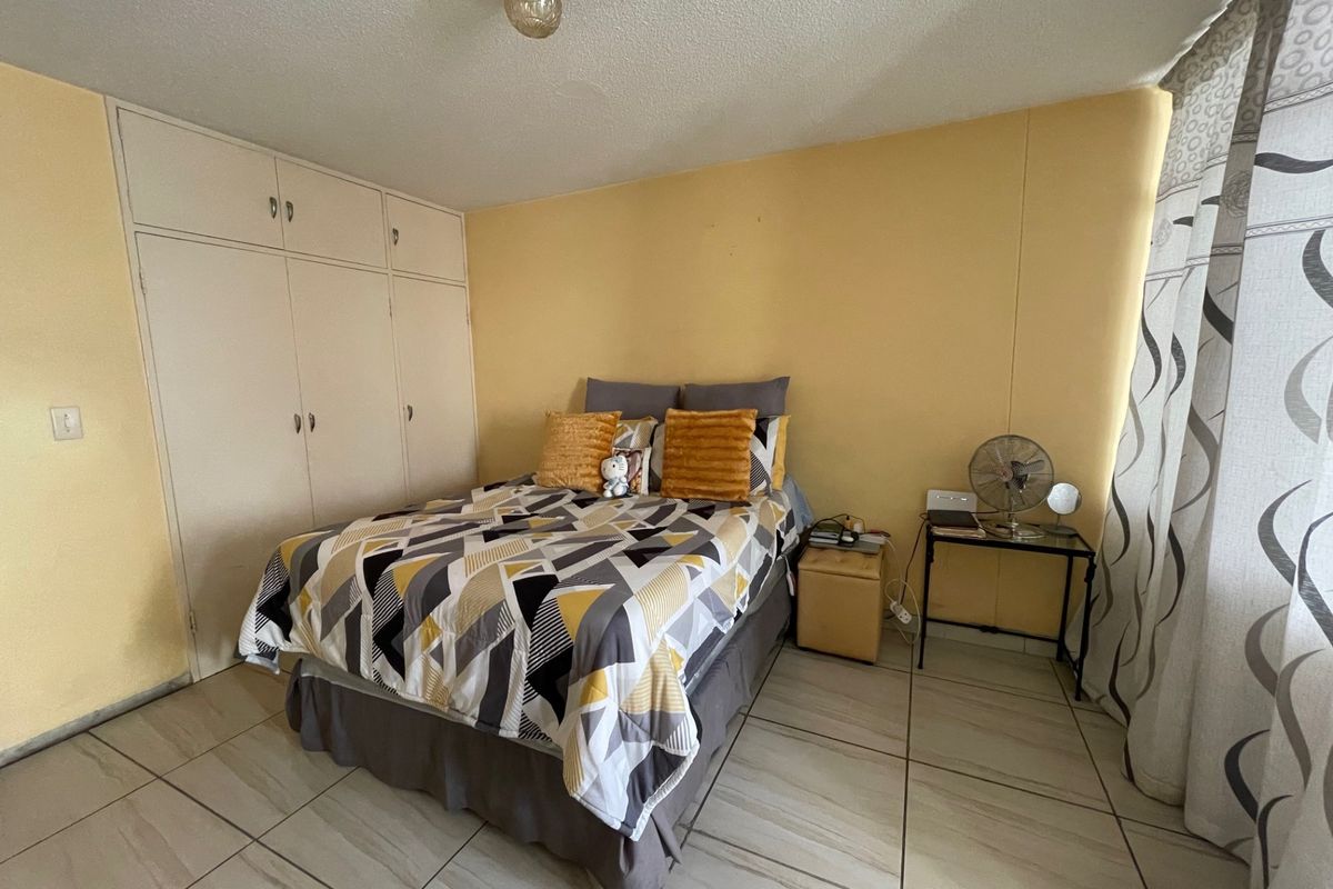 A bedroom featuring built-in cupboards, tiled flooring, and a ceiling light fixture, requiring cosmetic updates to the wall finishes.