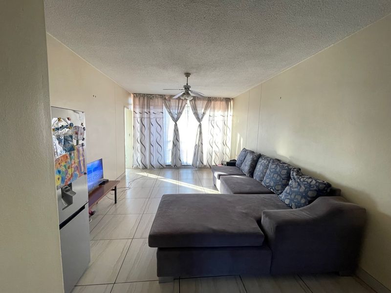 A spacious living area featuring tiled flooring, a ceiling fan, and large sliding glass doors that provide natural light.