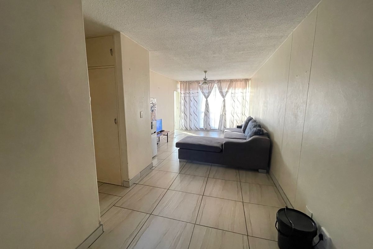 A living room area featuring tiled flooring, a ceiling fan, and a built-in storage cupboard, leading towards a window with curtains.