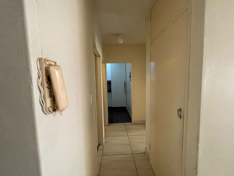 A functional hallway featuring tiled flooring, a built-in cupboard, and an integrated intercom system, leading towards an adjacent room.