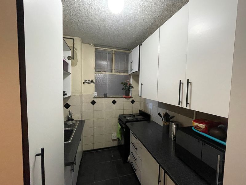 Compact galley-style kitchen featuring white cabinetry, dark countertops, tiled backsplash, and an electric stove, requiring some cosmetic updates to the walls and finishes.