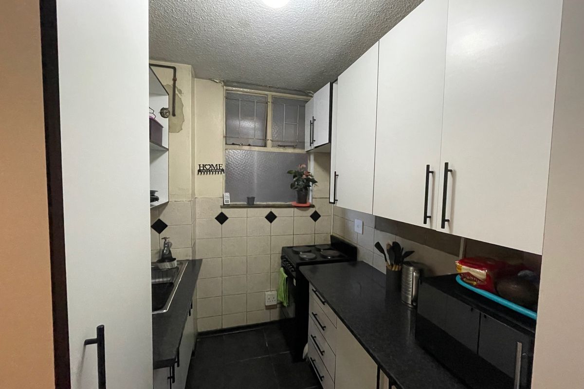 Compact galley-style kitchen featuring white cabinetry, dark countertops, tiled backsplash, and an electric stove, requiring some cosmetic updates to the walls and finishes.