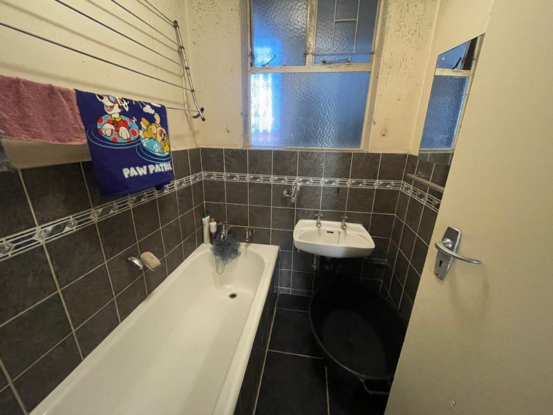 A dated bathroom featuring a bathtub, wall-mounted basin, and tiled finishes, currently requiring cosmetic updates and maintenance to the walls and ceiling.