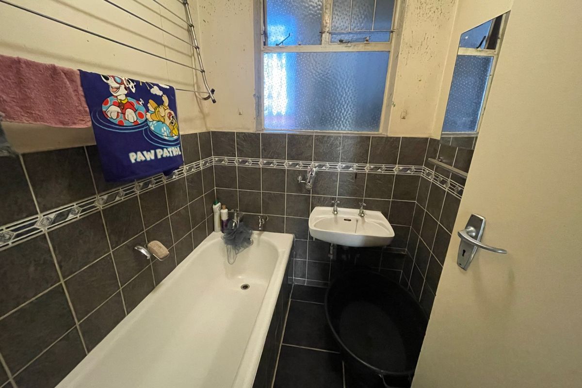 A dated bathroom featuring a bathtub, wall-mounted basin, and tiled finishes, currently requiring cosmetic updates and maintenance to the walls and ceiling.
