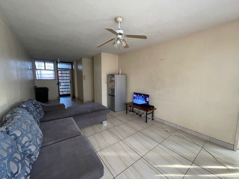A living area featuring tiled flooring, a ceiling fan, and access to a secure entrance, offering a functional space ready for cosmetic updates.