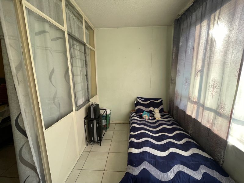 A compact bedroom featuring tiled flooring, a large window for natural light, and a partition wall structure.