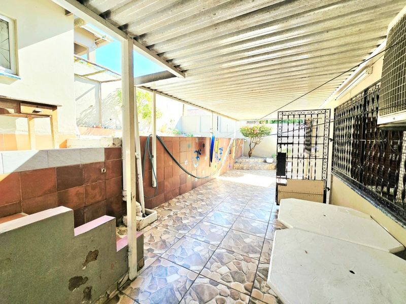 A covered outdoor patio area featuring tiled flooring, wall cladding, and a corrugated metal roof, providing a functional space for outdoor activities.