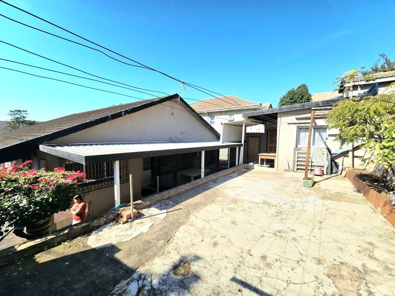Rear exterior view of the property featuring a concrete patio area, covered veranda, and security bars on windows.