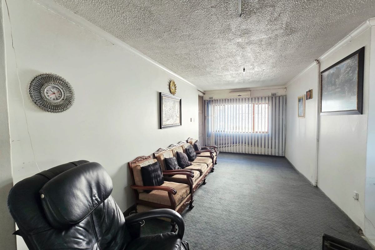 A living room featuring carpet flooring, a textured ceiling, and an air conditioning unit, with vertical blinds covering the window.