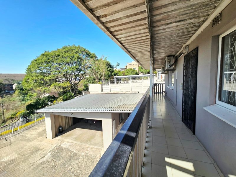 A covered balcony featuring tiled flooring, a metal railing, and a security gate, overlooking the driveway and garage area.