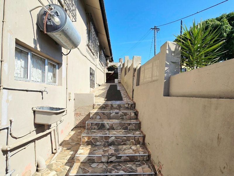 Exterior side passage featuring a tiled staircase, boundary wall, and utility sink with an externally mounted electric geyser.