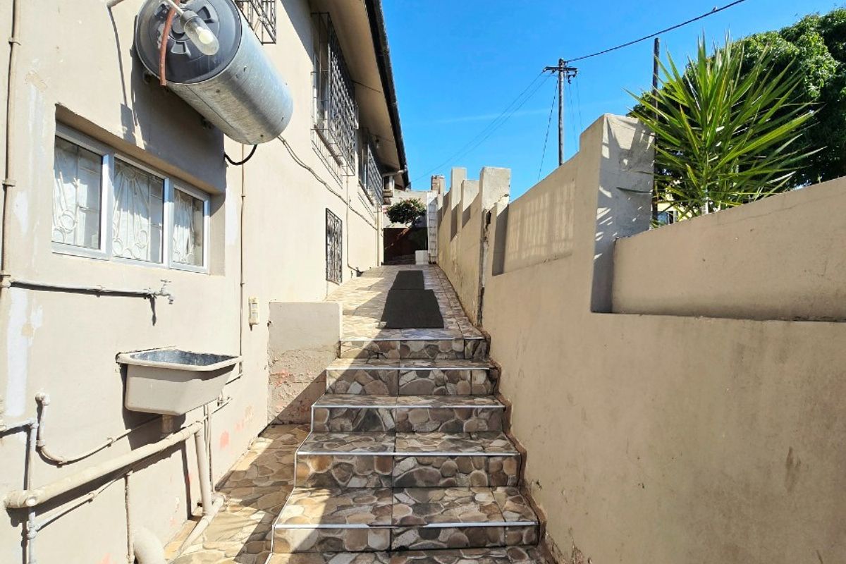 Exterior side passage featuring a tiled staircase, boundary wall, and utility sink with an externally mounted electric geyser.