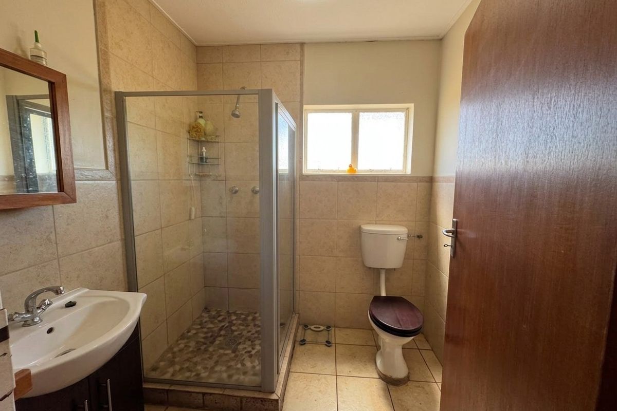 A functional bathroom featuring a glass-enclosed shower, vanity basin, and toilet with neutral ceramic tiling throughout.