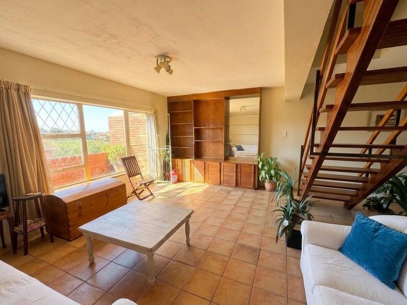 Spacious living room featuring a built-in wooden shelving unit, tiled flooring, and an open-tread wooden staircase leading to the upper level.