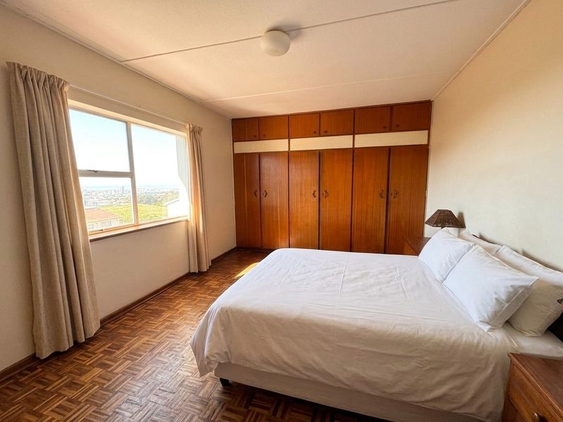 A well-lit bedroom featuring classic parquet flooring, extensive built-in wooden cabinetry, and a large window offering elevated views.
