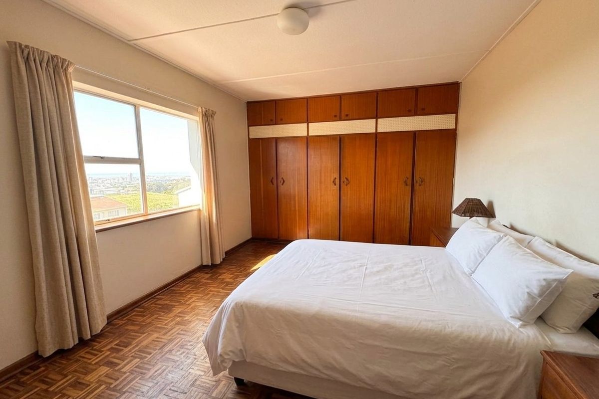 A well-lit bedroom featuring classic parquet flooring, extensive built-in wooden cabinetry, and a large window offering elevated views.