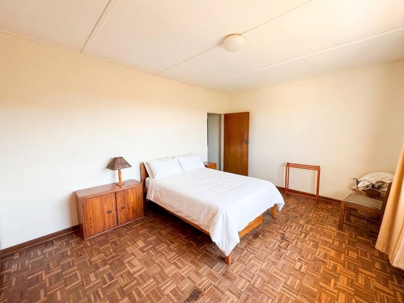A simple bedroom featuring traditional parquet flooring and neutral wall finishes, offering a functional space with potential for modern updates.