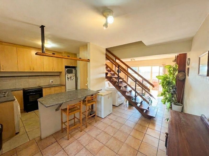 Open-plan kitchen and living area featuring a wooden staircase, granite breakfast bar, and tiled flooring throughout.