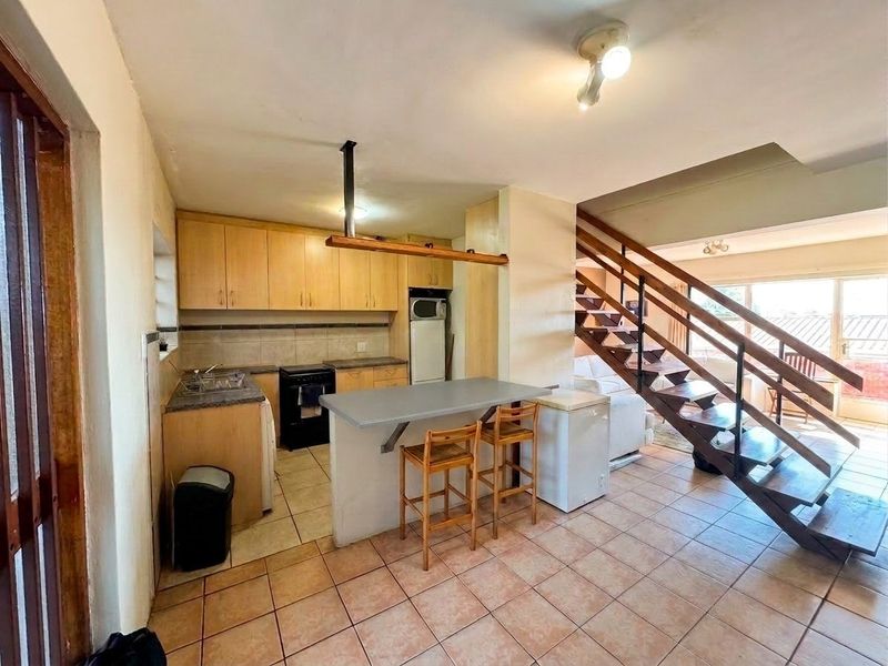 Open-plan kitchen and living area featuring wooden cabinetry, a breakfast bar, and a staircase leading to the upper level.