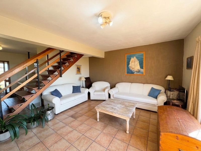 A spacious living room featuring ceramic tile flooring and an open-tread wooden staircase leading to the upper level.
