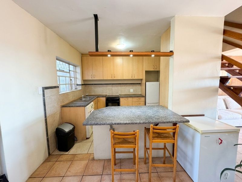 Functional kitchen featuring laminate cabinetry, granite breakfast bar, tiled backsplash, and ceramic flooring, with an open-plan layout adjacent to the staircase.