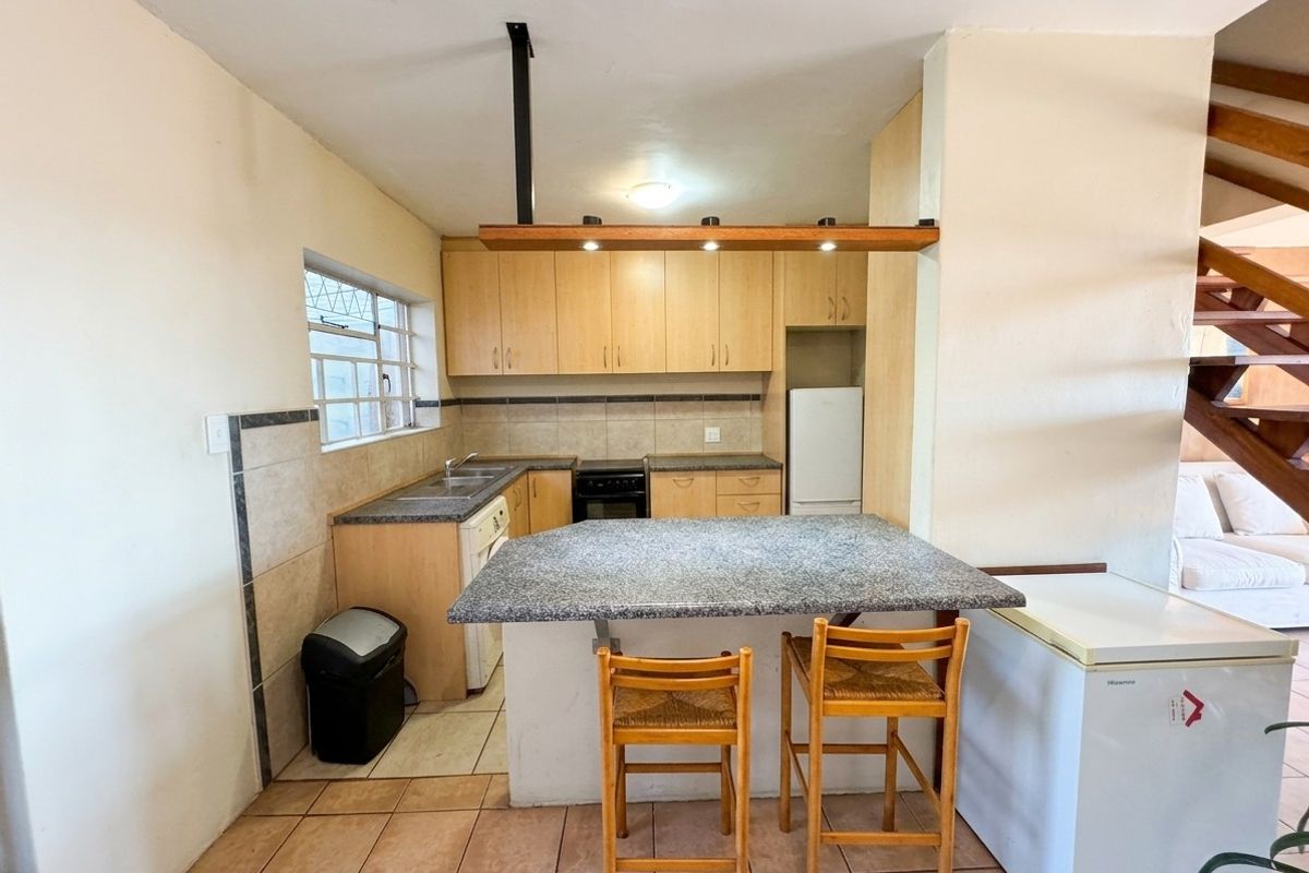 Functional kitchen featuring laminate cabinetry, granite breakfast bar, tiled backsplash, and ceramic flooring, with an open-plan layout adjacent to the staircase.
