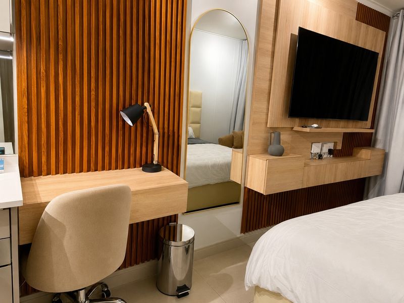 Modern bedroom featuring custom timber slat wall paneling, a built-in floating desk, and an integrated media console with a wall-mounted television.
