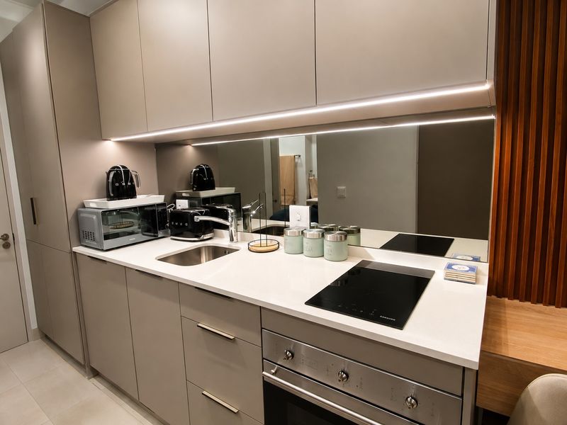 Modern, compact kitchen featuring sleek handleless cabinetry, stone countertops, a mirror splashback, integrated hob, and built-in oven with ambient under-cabinet lighting.