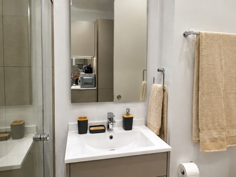 Modern bathroom featuring a sleek vanity cabinet with integrated basin, chrome fixtures, a large wall-mounted mirror, and a glass-enclosed shower.