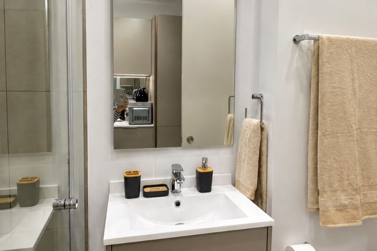 Modern bathroom featuring a sleek vanity cabinet with integrated basin, chrome fixtures, a large wall-mounted mirror, and a glass-enclosed shower.