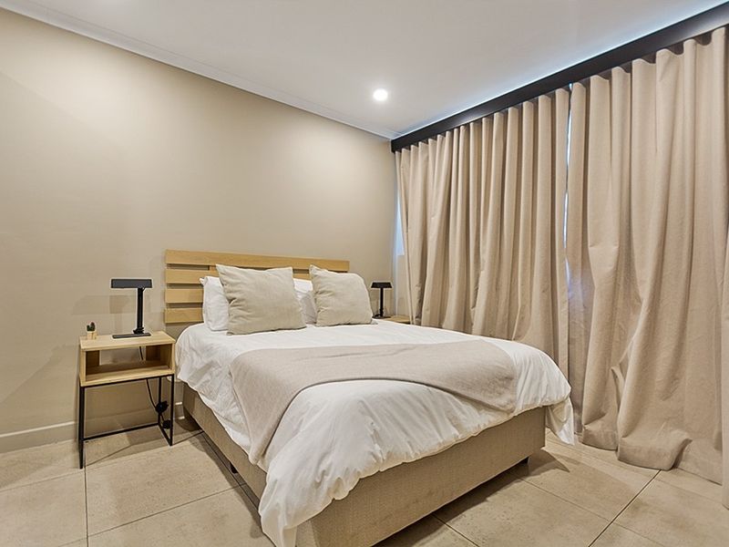 A well-maintained bedroom featuring neutral wall tones, tiled flooring, and floor-to-ceiling curtains.