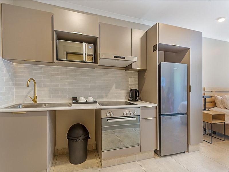 Modern compact kitchen featuring sleek taupe cabinetry, subway tile backsplash, integrated appliances, and a brass faucet, seamlessly integrated into an open-plan living space.