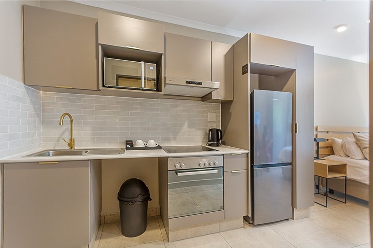 Modern compact kitchen featuring sleek taupe cabinetry, subway tile backsplash, integrated appliances, and a brass faucet, seamlessly integrated into an open-plan living space.