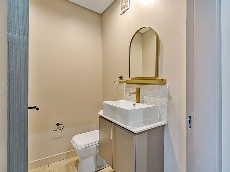 A modern, compact powder room featuring a sleek vanity with a vessel sink, brass fixtures, and an arched mirror.