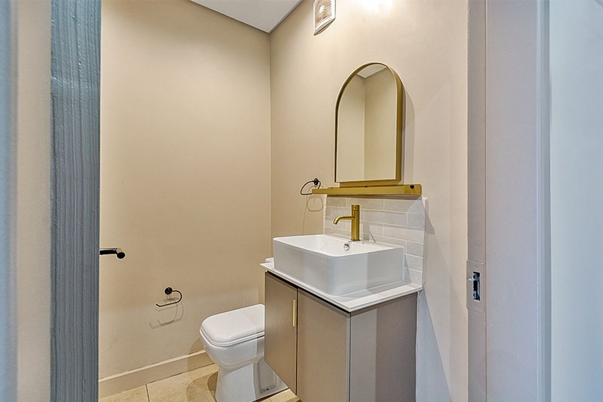 A modern, compact powder room featuring a sleek vanity with a vessel sink, brass fixtures, and an arched mirror.