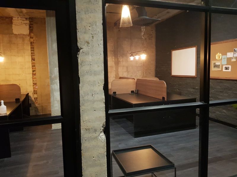 Industrial-style office space featuring exposed concrete columns, brickwork, and black metal-framed glass partitions with modern laminate flooring.