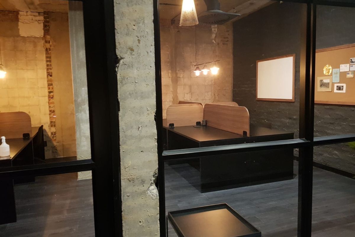 Industrial-style office space featuring exposed concrete columns, brickwork, and black metal-framed glass partitions with modern laminate flooring.