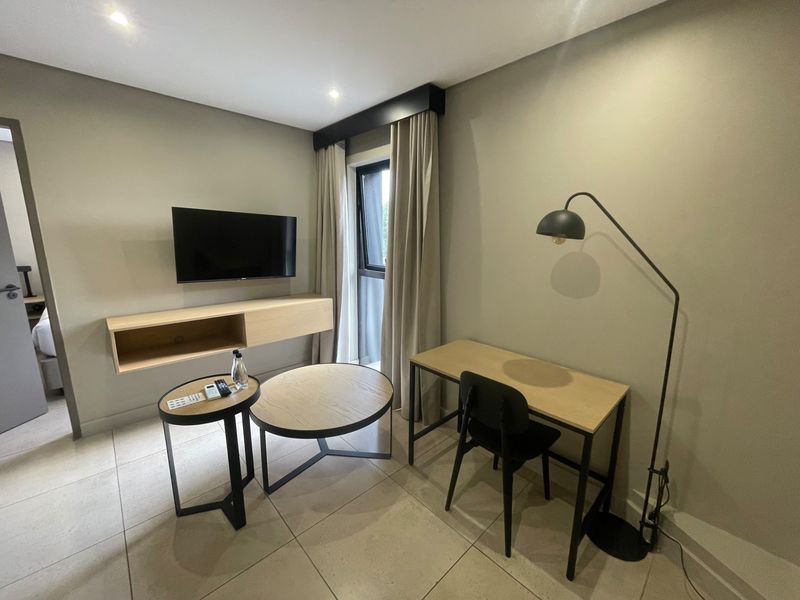 A modern bedroom featuring tiled flooring, recessed lighting, and a wall-mounted media console, offering a clean and contemporary living space.