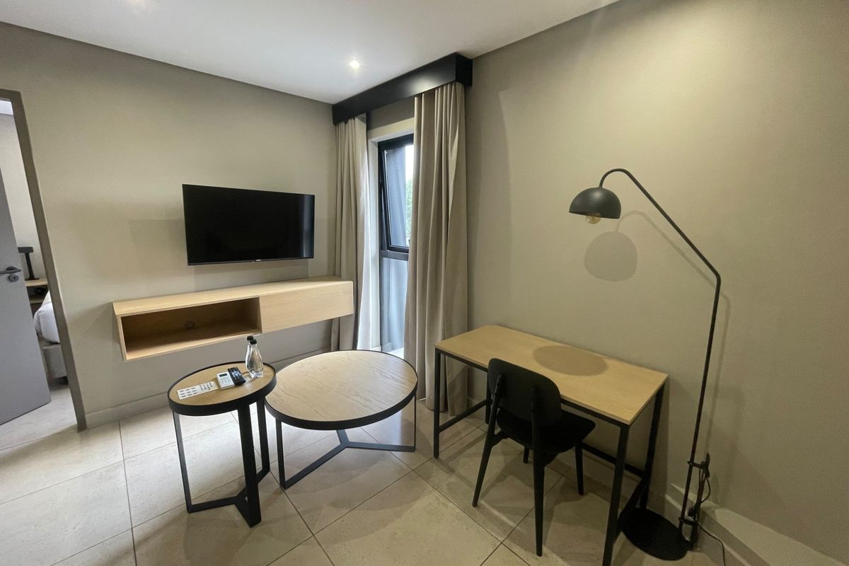 A modern bedroom featuring tiled flooring, recessed lighting, and a wall-mounted media console, offering a clean and contemporary living space.
