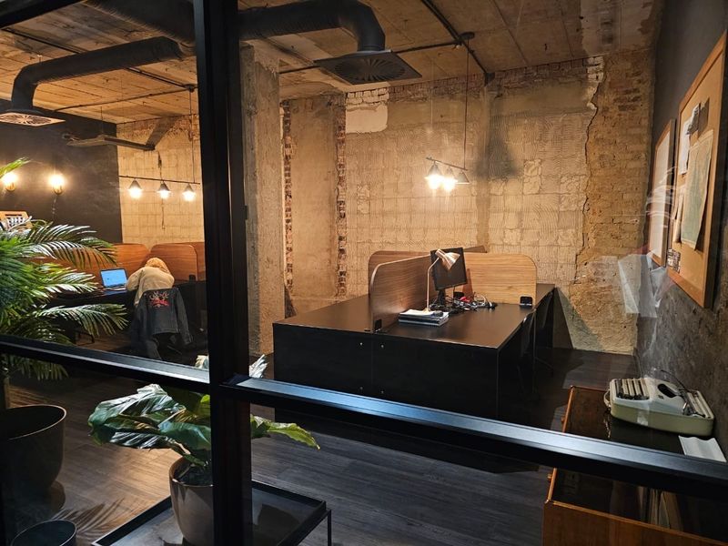 Industrial-style office space featuring exposed brick walls, concrete ceilings, and black metal-framed glass partitions, creating a modern, raw aesthetic.