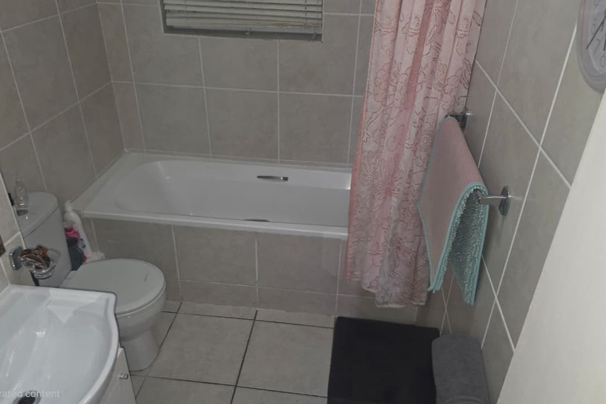 A functional bathroom featuring a bathtub, pedestal sink, toilet, and neutral wall and floor tiling.