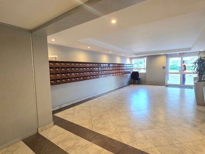 A spacious apartment building entrance lobby featuring tiled flooring, recessed lighting, and a wall of built-in mailboxes for residents.