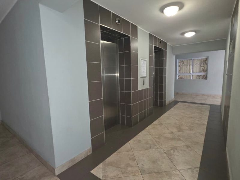 A clean and well-maintained apartment building hallway featuring tiled flooring, elevator access, and secure entry points.