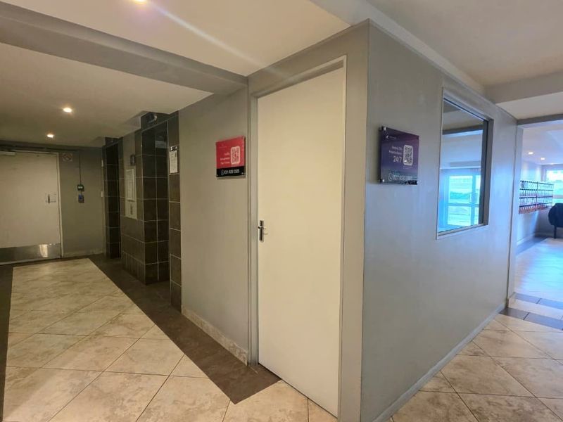 A clean and well-maintained apartment building hallway featuring tiled flooring, recessed lighting, and access to the elevator.