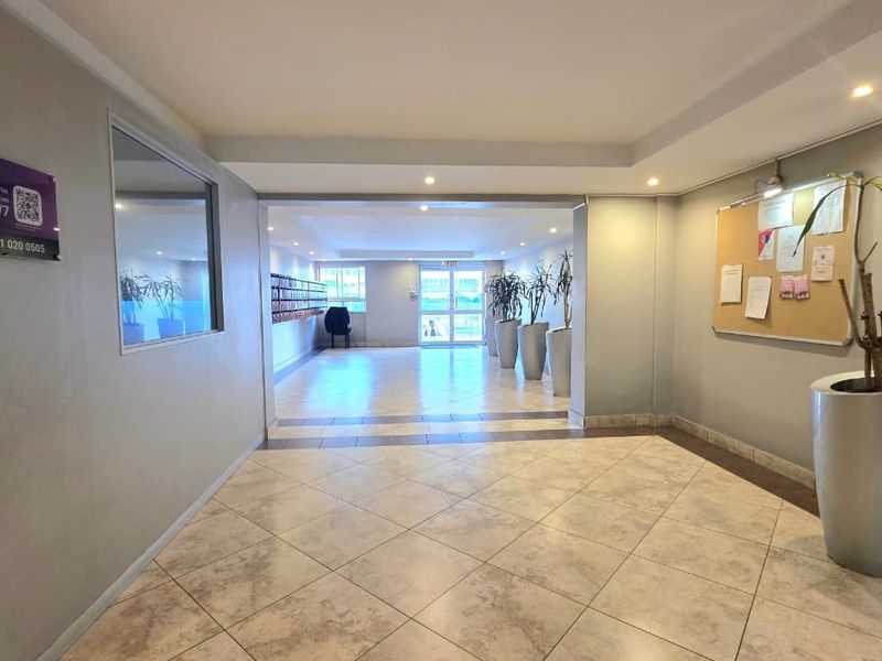 A clean and well-maintained apartment building entrance lobby featuring tiled flooring, recessed lighting, and a communal mailbox area.