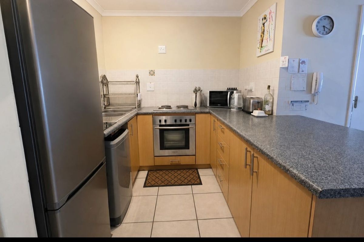 A functional kitchen featuring light wood cabinetry, granite-look laminate countertops, a built-in oven, electric hob, and tiled flooring.