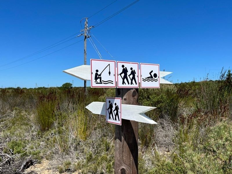 A wooden directional signpost indicating recreational activities such as fishing, hiking, and swimming, situated in a natural, undeveloped landscape.